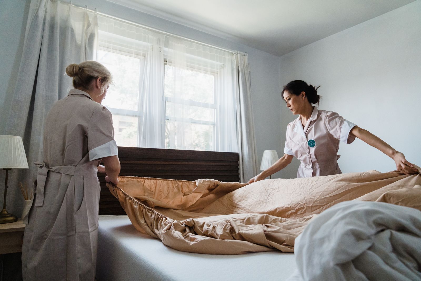 Two professional housekeepers making up a bedroom with fresh linen